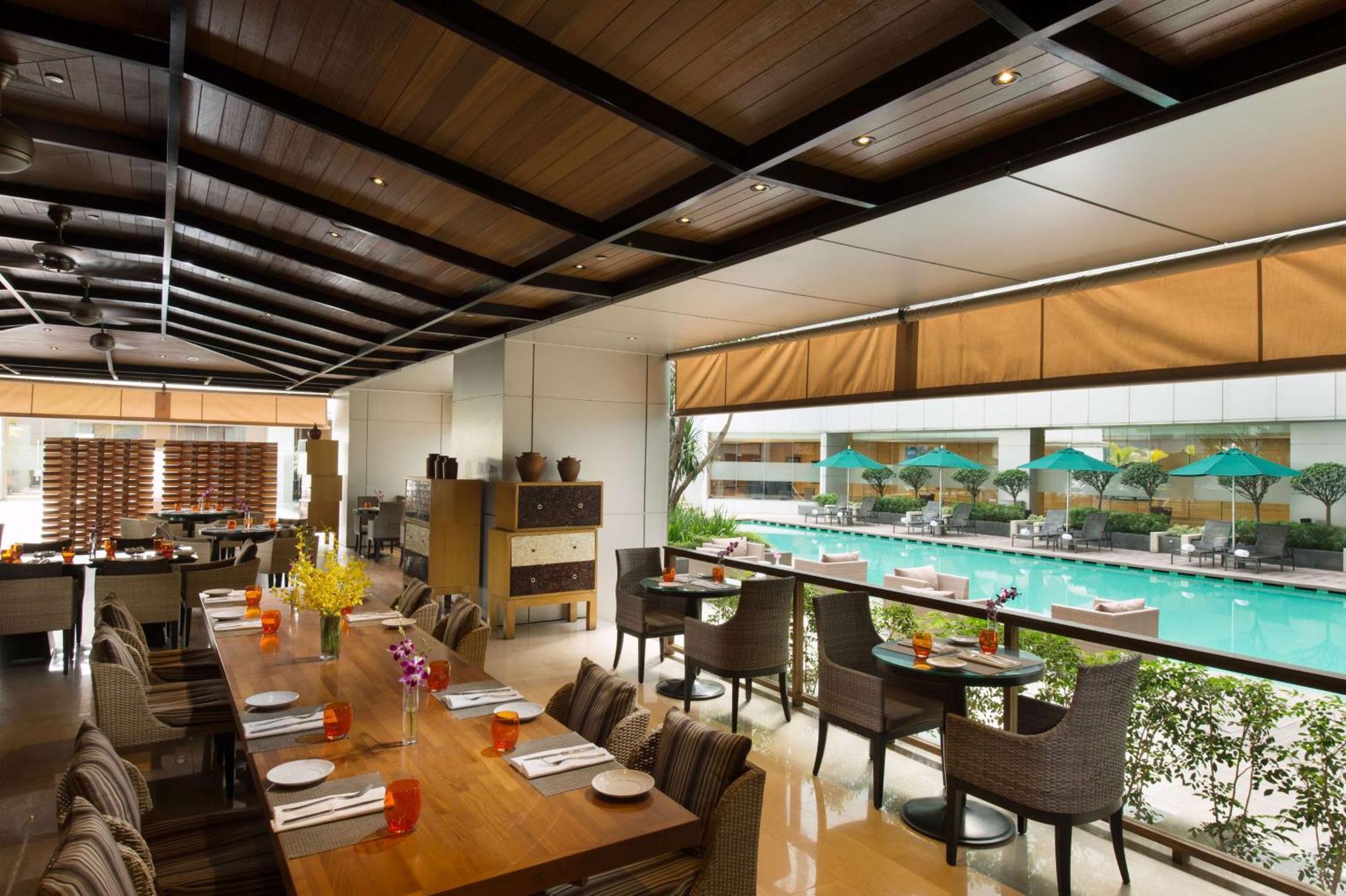Doubletree By Hilton Kuala Lumpur Ξενοδοχείο Εξωτερικό φωτογραφία The photo shows an indoor restaurant area with a modern and stylish design. There are several tables set for dining, featuring place settings and drinks. Large windows allow for a view of a swimming pool outside, which is adorned with umbrellas. The 
