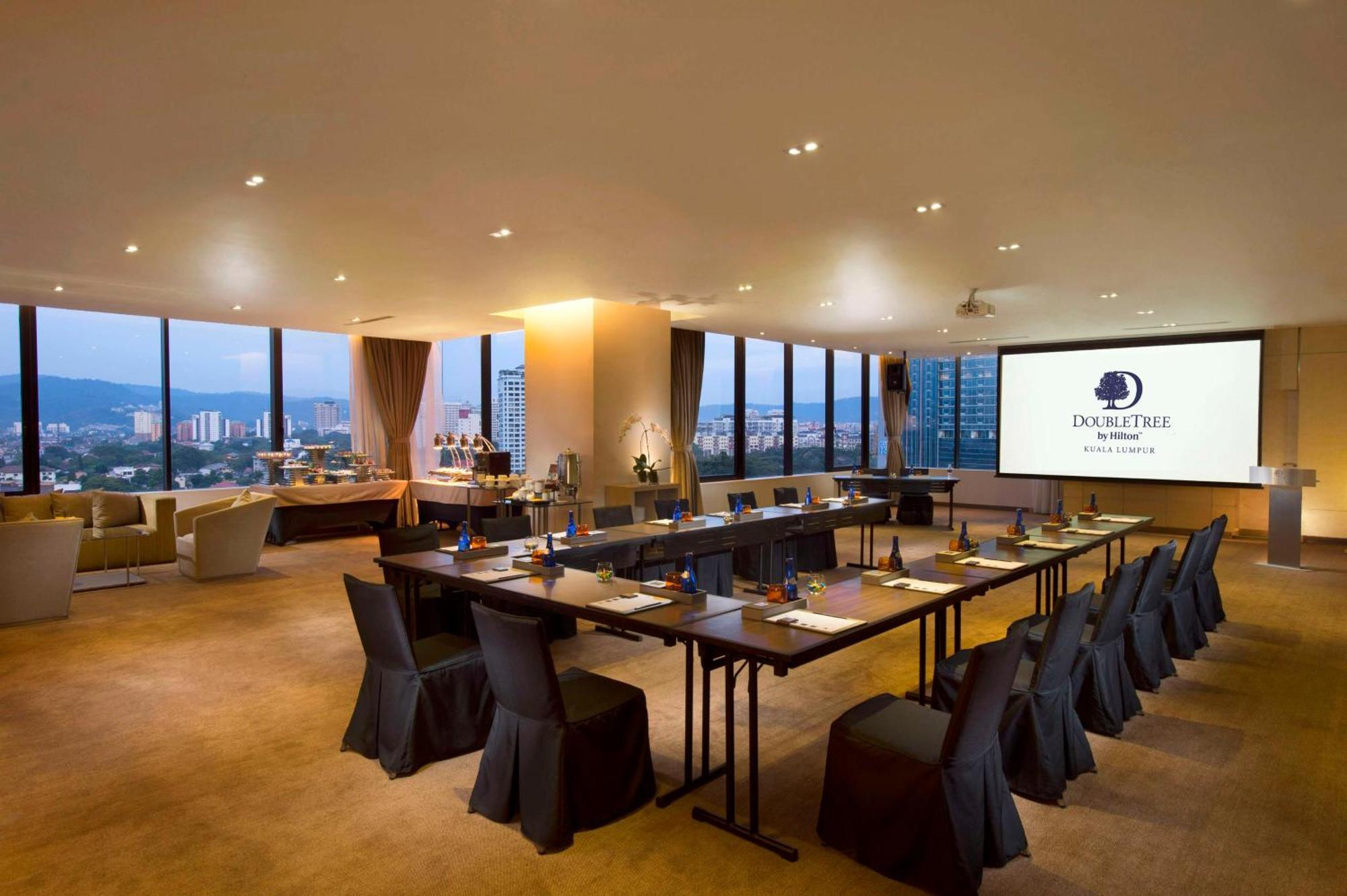 Doubletree By Hilton Kuala Lumpur Ξενοδοχείο Εξωτερικό φωτογραφία The photo shows a modern conference room. It features a long table arranged for a meeting, with black chairs and notepads placed at each seat. The room has large windows that let in natural light and offer a view of the city outside. On one wall, the